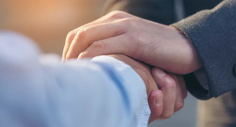 Eine Hand liegt auf den ineinandergelegten Händen zweier Menschen.